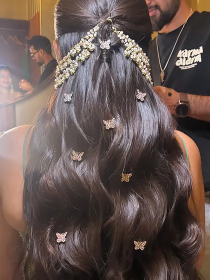 A whimsical and romantic half-up style with soft waves. The look is adorned with a beautiful hairpiece and scattered butterfly clips, perfect for a fun event like a Mehendi or Qawwali night.