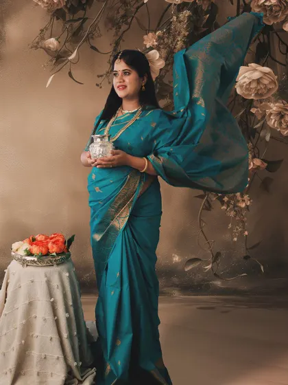 A fine art maternity portrait in a teal saree. The painted floral backdrop and soft lighting give this image a dreamy, painterly quality.