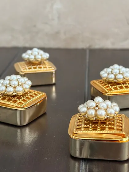 A close-up of my classic pearl-topped coin boxes. The intricate design on the golden box and the luster of the pearls make this a truly elegant shagun gift.