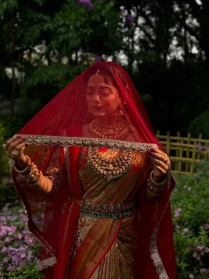 A mysterious and beautiful shot of a South Indian bride under a red veil. The golden saree glows, and the drape is impeccable.
