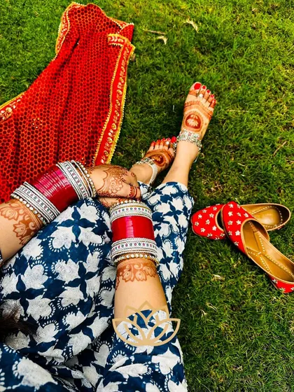 A creative shot showcasing the beautiful henna stain on both hands and feet, complemented by traditional red bangles and juttis.