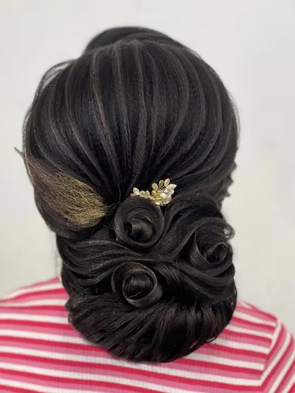 This updo features multiple hair roses crafted into a low bun. The golden accessory adds a touch of warmth and elegance to this highly detailed hairstyle.