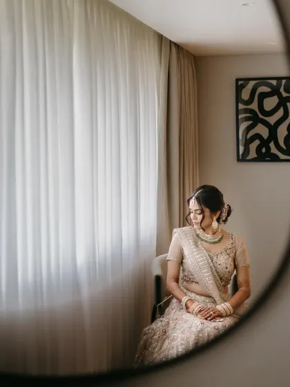 An artistic shot of a bride reflected in a round mirror, creating a moody and introspective portrait as she sits by a window.