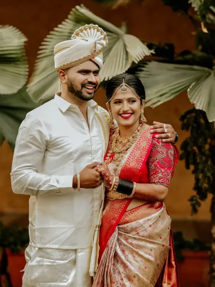 A classic portrait of a South Indian couple on their wedding day, their coordinated white and red outfits glowing with happiness.