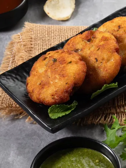 A close-up of Aloo Tikki, focusing on the crispy texture of the potato patties. The simple styling with mint chutney keeps the focus on this classic snack.