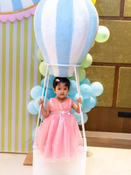 A little girl in a pink dress stands inside a hot air balloon prop at her third birthday party. We look for fun and interactive photo opportunities that make the kids' party photography session enjoyable.