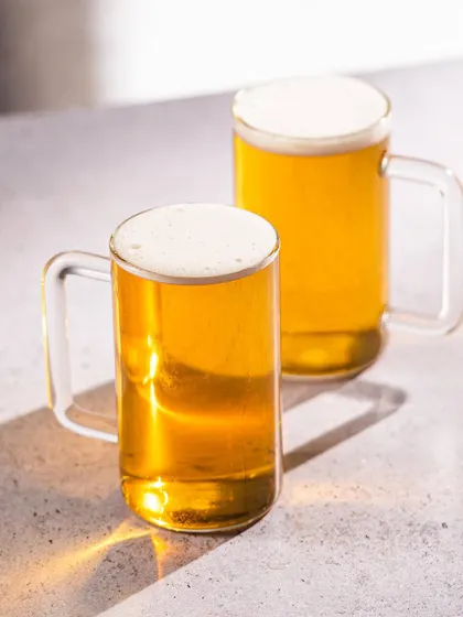 Clean product photography of classic beer mugs. The bright, hard light creates sharp reflections, highlighting the clarity of the glass and the color of the beer.