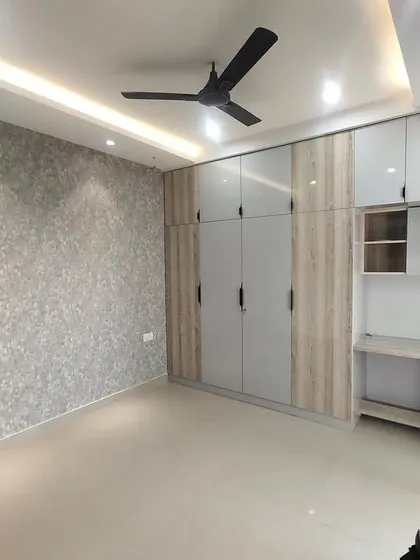 A finished bedroom with a full-wall wardrobe and an integrated study unit. The combination of grey and wood-grain laminate, along with a textured wallpaper, creates a sophisticated and functional space.