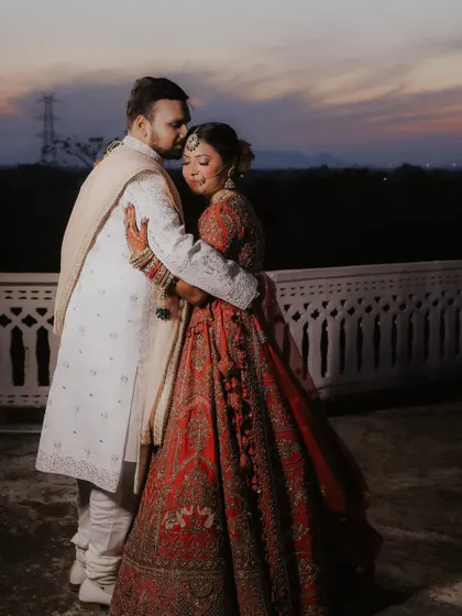 A tender embrace as the sun sets over Jaipur. This candid shot focuses on the quiet connection between the couple, with the beautiful twilight sky adding a touch of natural drama to their royal portrait.