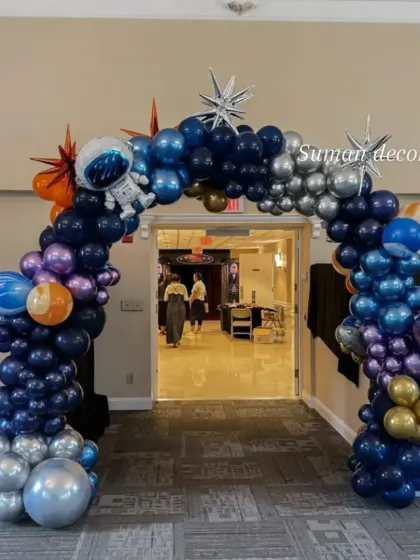 A space-themed balloon arch perfect for a party entrance. This arch is made with dark blue, purple, and silver balloons and decorated with astronaut and star cutouts.