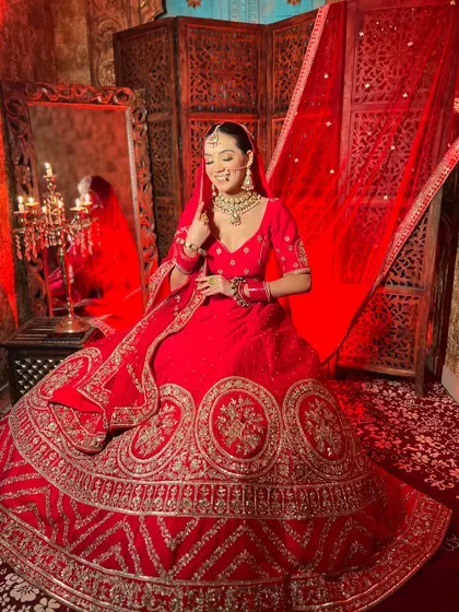 A smiling bride in a classic red lehenga. The rich color and detailed gold embroidery create a joyful and celebratory look, perfect for your wedding photos.