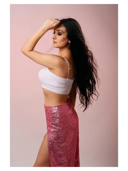 A soft and feminine portrait against a pink studio background. The flowing hair and sequined skirt create a glamorous and dreamy atmosphere.