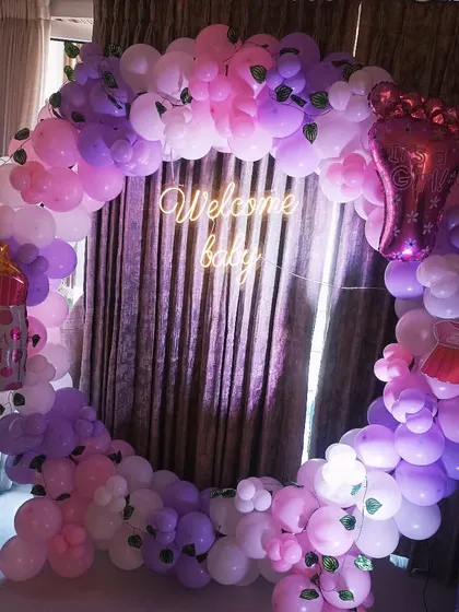 This full balloon ring in shades of pink and purple is perfect for a baby girl's shower. I added fun foil balloons like a baby bottle and a tiny foot, along with a 'Welcome baby' neon sign.