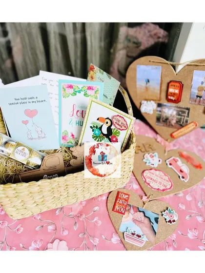 A creative and personal gift set including a basket of treats and cards, alongside custom heart-shaped cork boards decorated with photos and stickers.