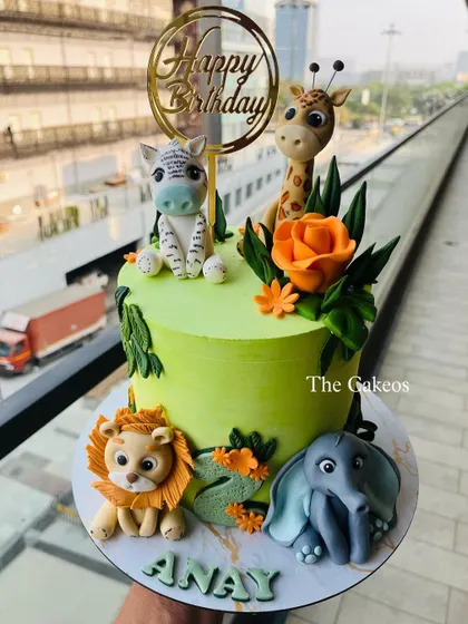 A vibrant green jungle cake with four adorable fondant animals: a lion, elephant, giraffe, and zebra. Orange sugar flowers add a pop of color to this fun safari design.
