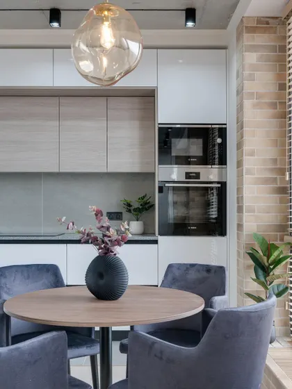 The open kitchen and dining space in our minimalist apartment design, where natural textures like brick and wood meet sleek, modern cabinetry.
