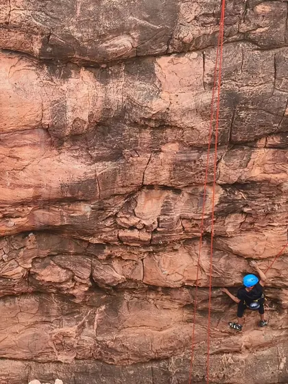 A climber is dwarfed by the immense scale of the rock wall in Badami.