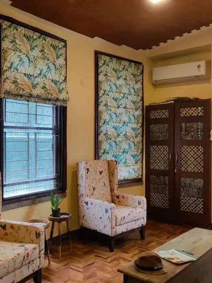 A quiet corner of a home where everything is in its place. The custom floral-patterned Roman blinds and matching wingback chairs create a cohesive and restful interior, complemented by the warm tones of the parquet flooring.