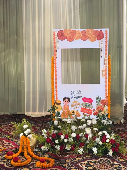 A custom photo booth frame for the Haldi ceremony. The frame is decorated with flowers and illustrations, providing a fun prop for guest photos.