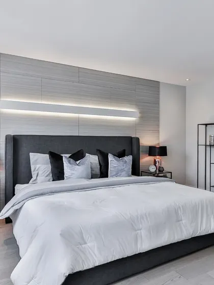 Elegance is in the details. This bedroom showcases a clean, modern aesthetic with a textured feature wall, integrated horizontal lighting, and a minimalist color palette of grey and white for a calm and comfortable feel.