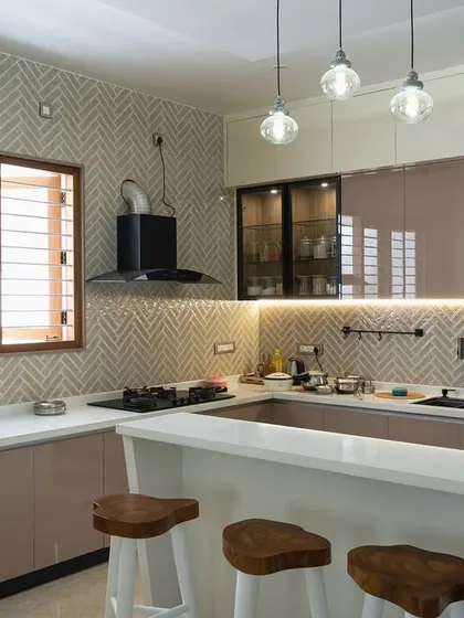 A spacious and elegant kitchen with a breakfast bar. The design features beige and glass cabinets, a herringbone backsplash, and stylish pendant lights, combining functionality with high-end aesthetics.