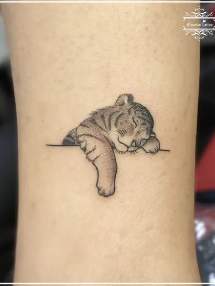An adorable sleeping tiger cub tattoo. This piece shows our softer side, capturing a moment of peace and innocence with delicate shading and fine lines.