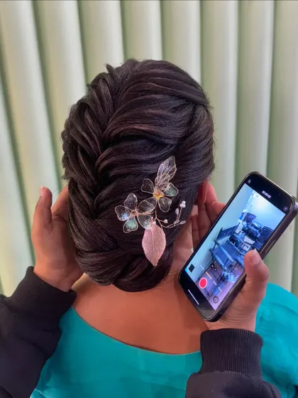 A student capturing their work on camera. This beautiful braided bun with a floral accessory is a result of their dedicated practice.