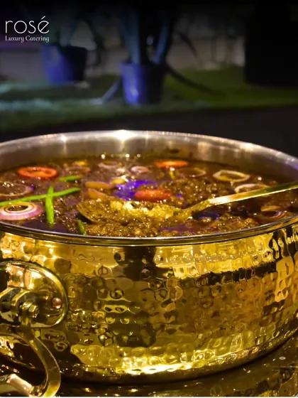 A close-up of a rich, dark curry in a hammered gold-tone bowl. We specialize in a wide range of Indian main courses, each prepared with authentic spices and slow-cooking techniques.