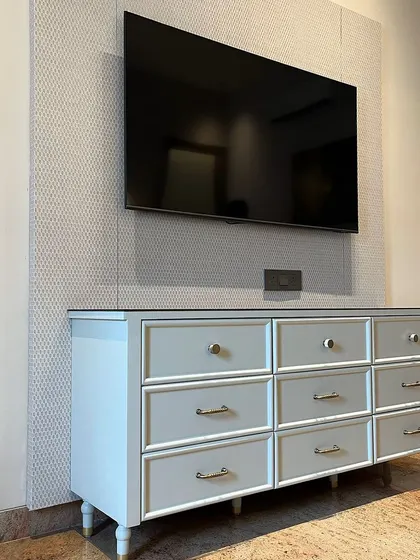 For this parent's room in Ambala, we designed a custom chest of drawers in a soft grey PU finish. It sits before a textured wallpaper panel that also serves as a backdrop for the television.