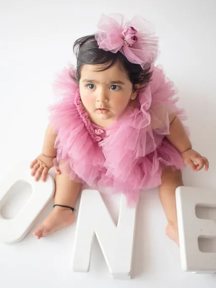 A birthday girl in a fluffy pink tulle dress poses with "ONE" letters against a clean white background.