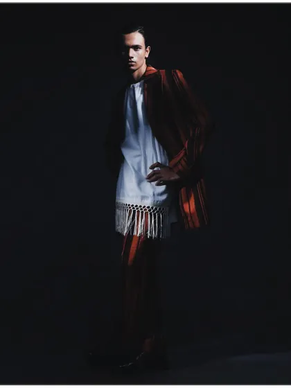 A classic portrait pose from the 'Silhouette' series, with the model standing against a dark background. The lighting is carefully controlled to highlight the contours of the suit and the subject's form.