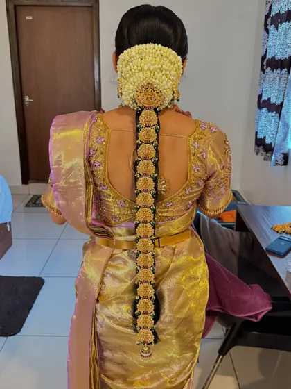 The back view of Hamsa's hairstyle, showcasing a traditional braid adorned with jasmine flowers and a golden accessory. This is a classic South Indian bridal hairstyle.