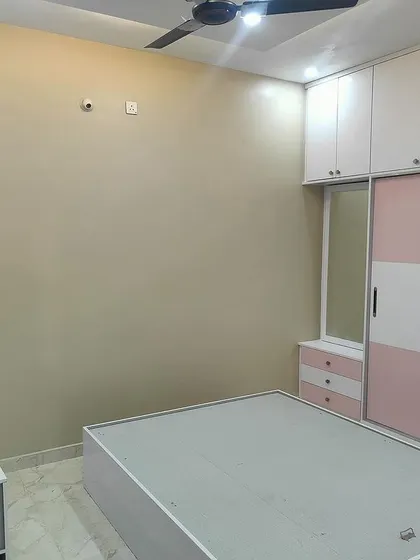 A bright and cheerful bedroom designed for a younger family member, with a pink and white color palette for the wardrobe and study unit. The space is functional, organized, and personalized.