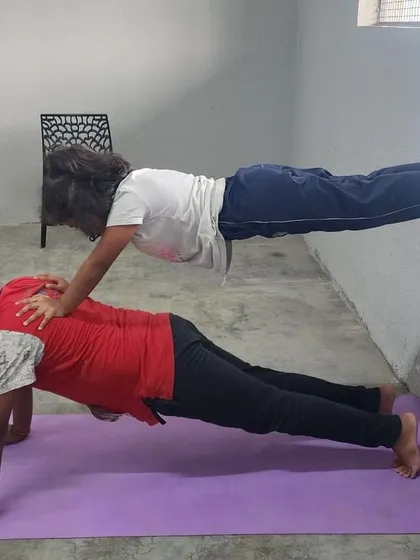 This partner plank variation shows a different hand placement, adapting the pose to suit the campers' comfort and strength.