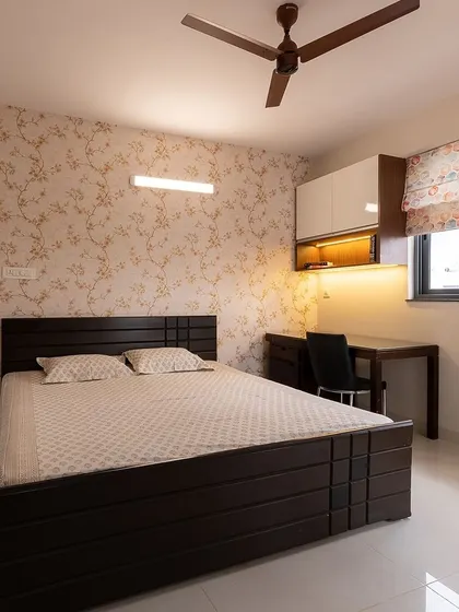 A cozy bedroom with dark wood furniture and floral wallpaper. An integrated study desk by the window makes this a practical and comfortable space for both rest and work.