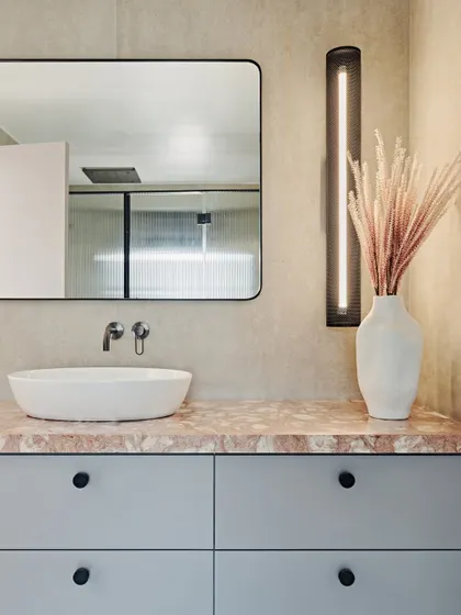 Each bathroom in the Maximum City Duplex has its own personality. This one features a soft, pastel color palette with a pink marble countertop, grey cabinetry, and a modern, linear wall light.