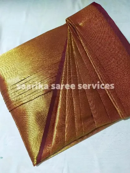 A shimmering tissue saree in a bronze shade, pleated and ready. I take special care with delicate fabrics to ensure they are not damaged.