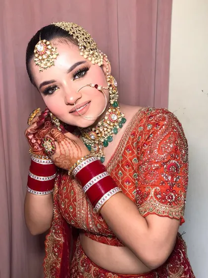 A close-up of Bhoomi's radiant bridal makeup. The look features soft shimmer on the eyes and a classic red chooda, perfectly complementing her orange and red lehenga.