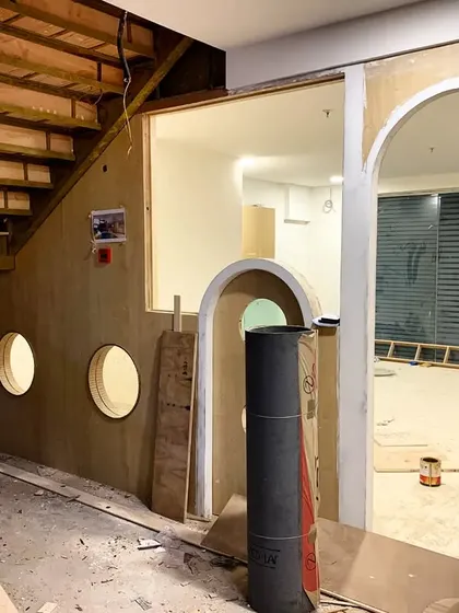 A view of the plywood structure under construction, with porthole windows and a wooden staircase taking shape.