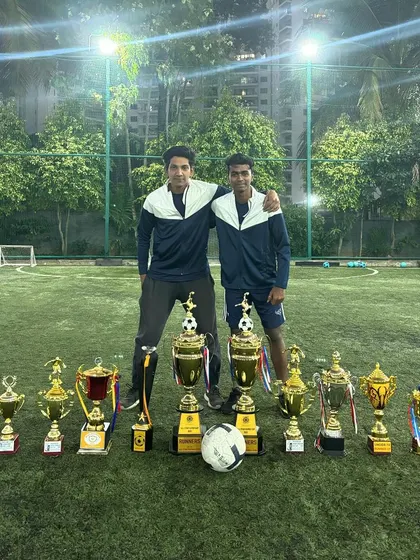 Two of our head coaches standing proudly with the trophies our teams have won. Our success is a team effort.