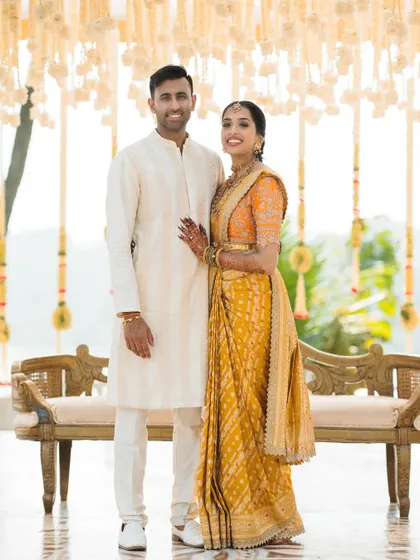 A classic, full-length portrait of the couple in their elegant South Indian wedding attire, standing before a beautifully decorated backdrop.