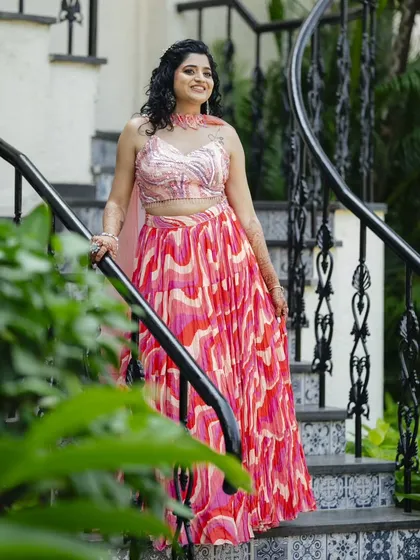 The bride posing on a staircase, her vibrant Haldi outfit in full view. The hairstyle is playful and pretty, perfect for the occasion.