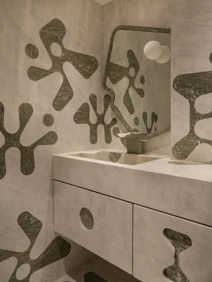 This powder bathroom is a bold play of geometry, where the marble walls and vanity are inlaid with organic, amoeba-like motifs in a contrasting stone.