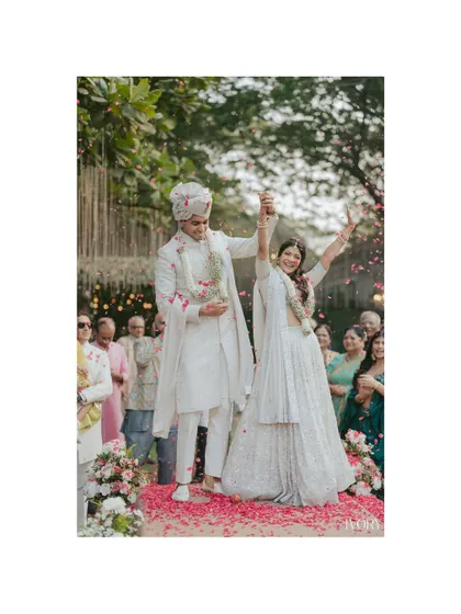 The celebration of a lifetime begins. This shot captures the couple's triumphant moment post-Varmala, hands raised in joy amidst a rain of petals from their loved ones.