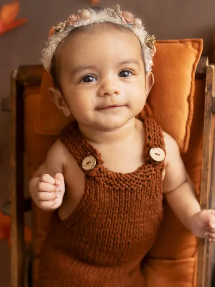 A sweet, happy smile. This 3-month-old, in her cozy knitted romper, is ready for her autumn-themed photoshoot.