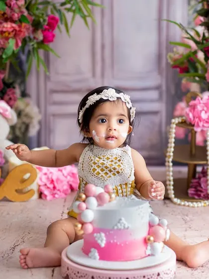 Getting right into the spirit of the celebration! This little one is enjoying her floral-themed first birthday cake smash, surrounded by beautiful props and teddy bears.