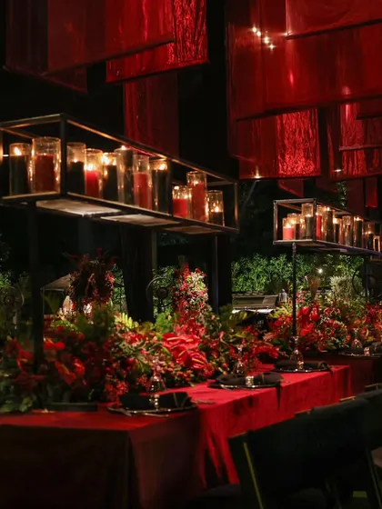 An intimate long table setting under a ceiling of suspended red fabric and candles. This design created a warm, enclosed, and deeply romantic atmosphere for guests.