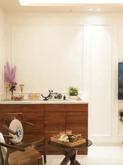 We designed this custom wooden crockery unit to provide storage while adding warmth to the white-themed living room. The classic wooden chairs create a charming corner for conversations.