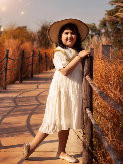 A stylish portrait of a young girl in a sunhat, posing on a rustic wooden bridge during a golden-hour shoot.