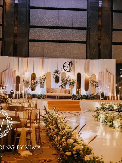 A classic and elegant reception setup symbolizing everlasting love. The stage features a modern, minimalist backdrop with custom monograms, floral arrangements, and soft lighting.